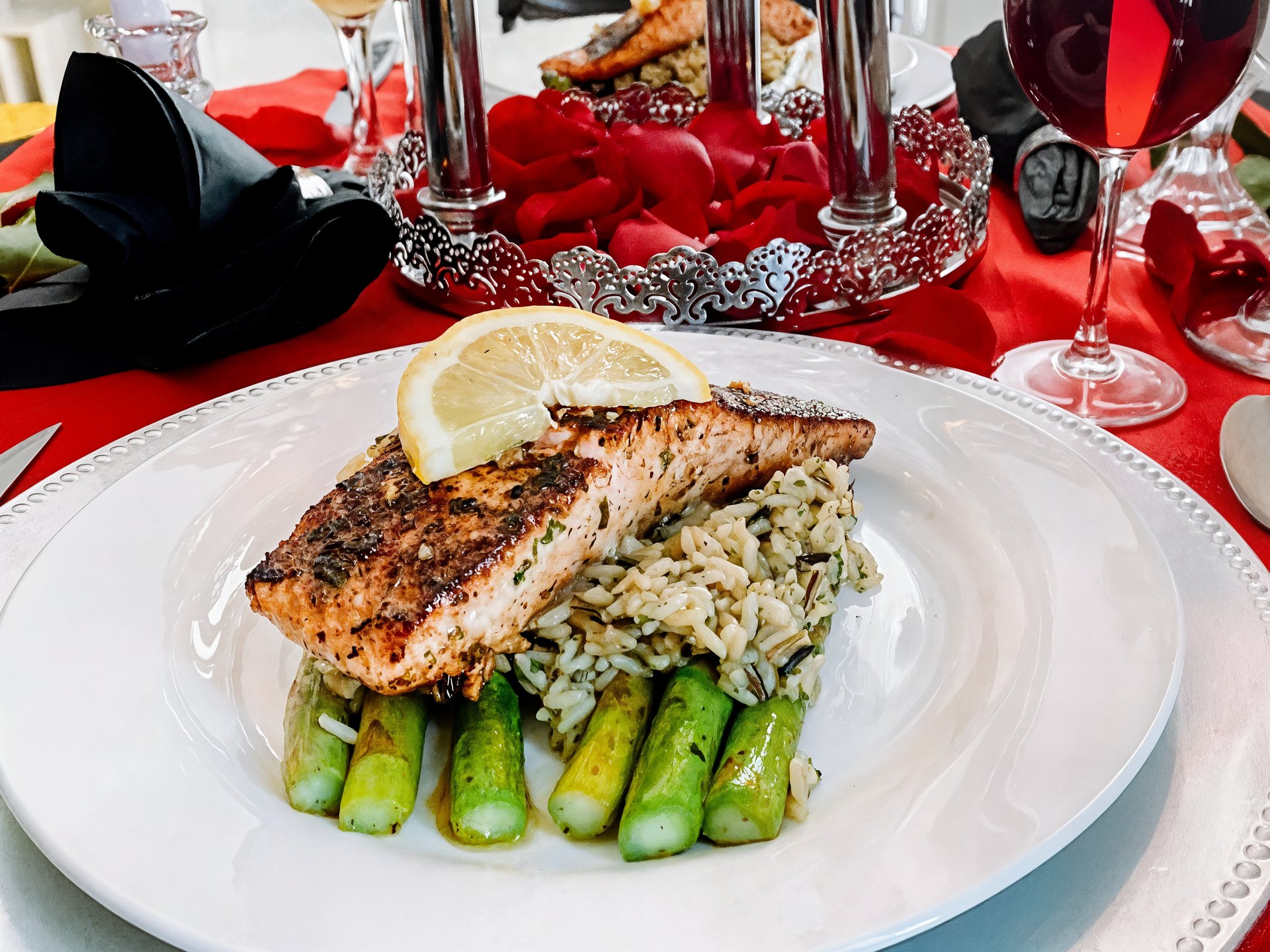 Seared salmon over wild rice and asparagus, plated for a romantic candlelit dinner with wine and rose petals